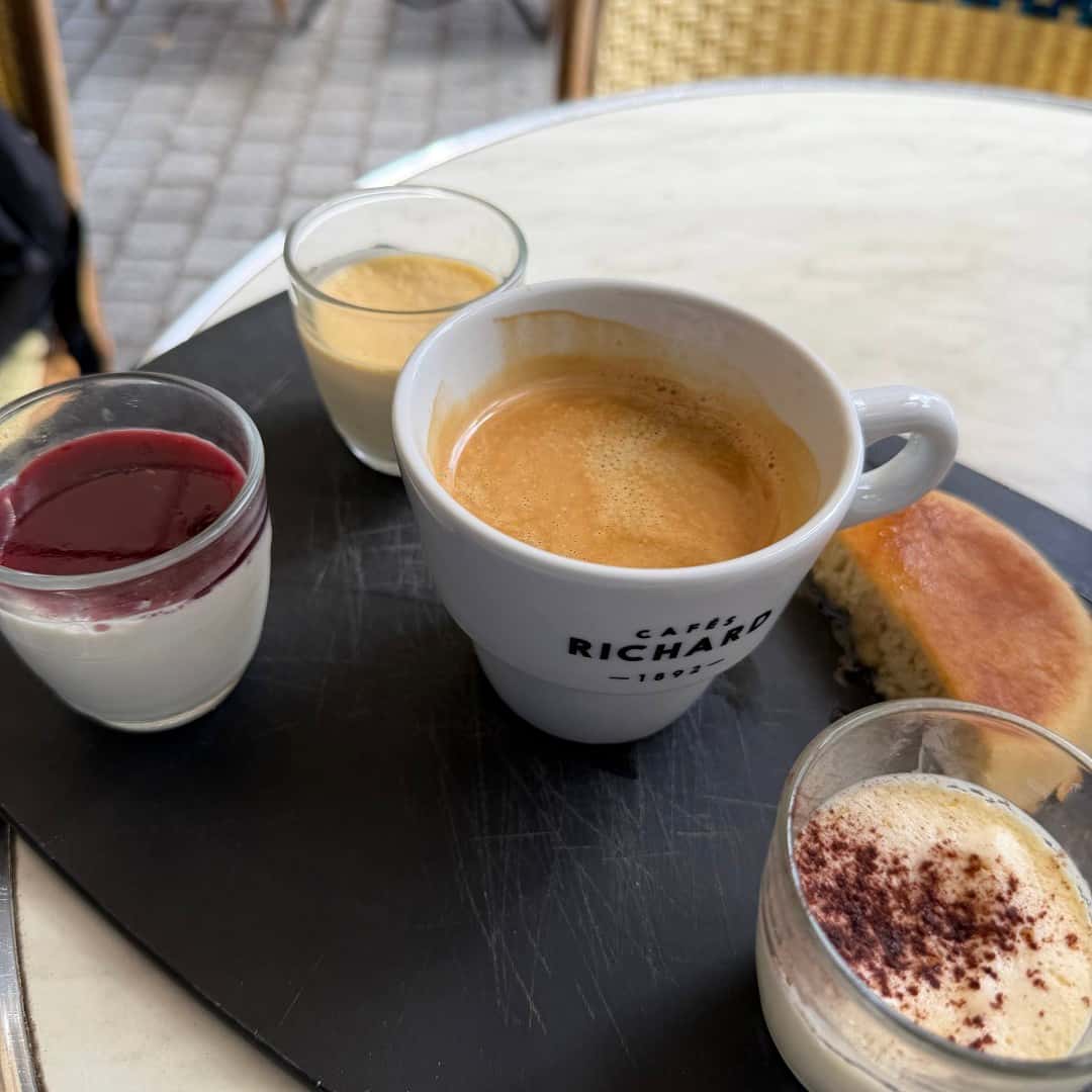 Phone photograph of a café gourmand with coffee, desserts, and cake on a black serving slate