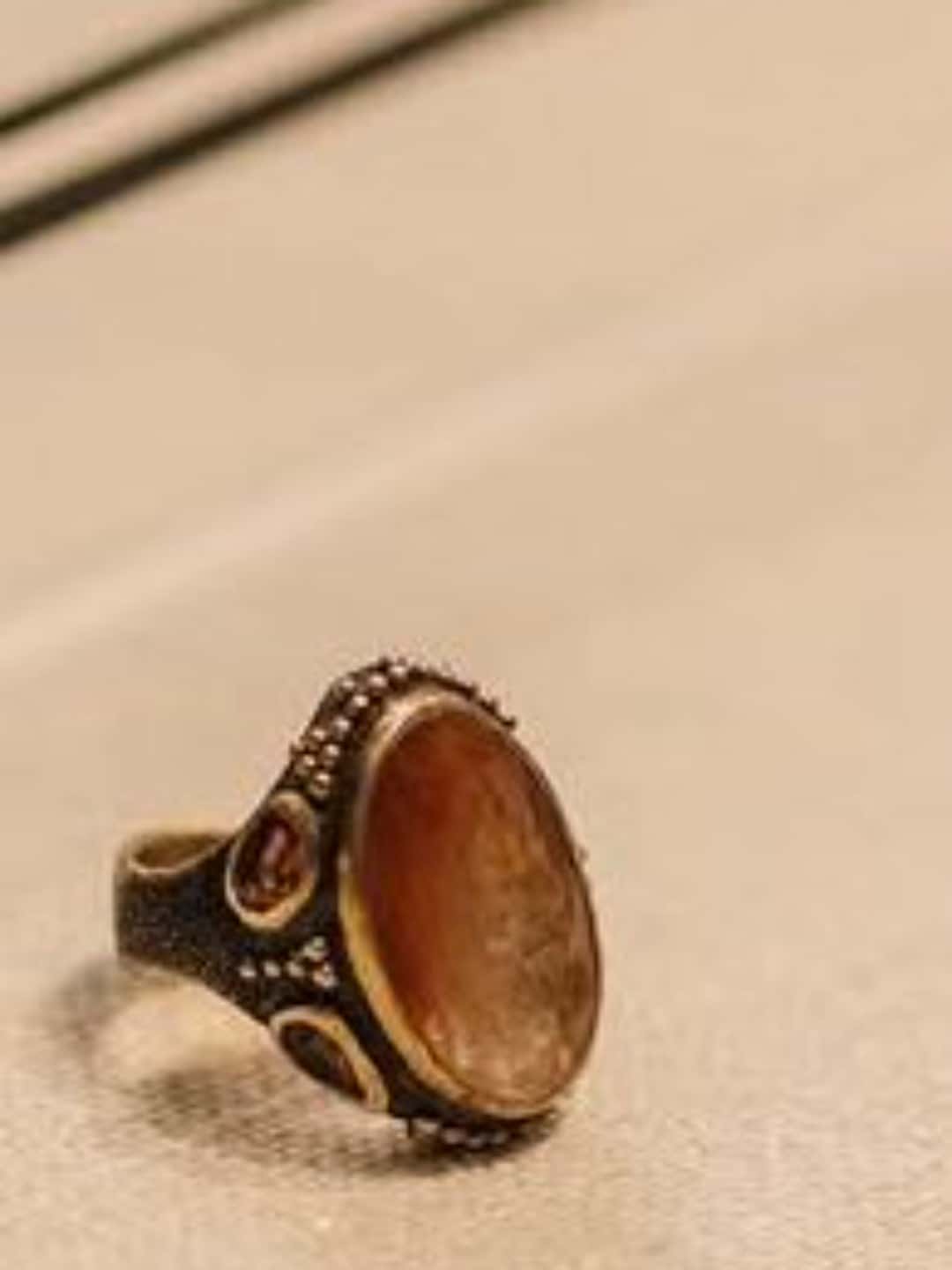Phone photograph of an amber-stone ring standing on a pale fabric surface