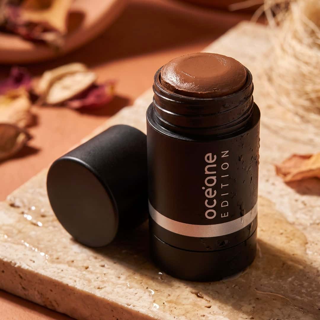 Art-directed close-up of the same black makeup stick on wet pale stone among dried leaves