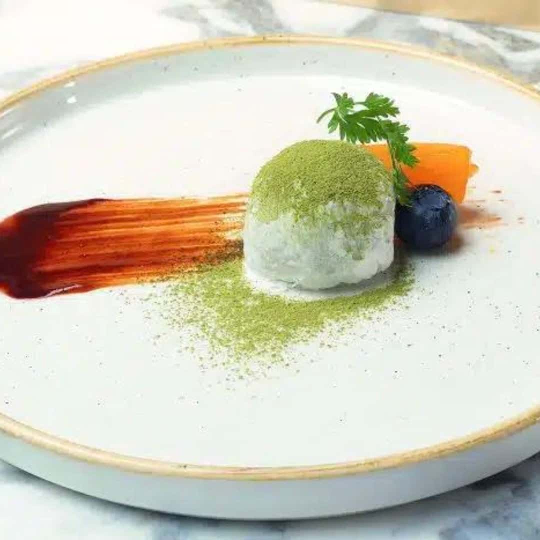 Phone photograph of a matcha-dusted dessert with fruit and sauce on a white plate