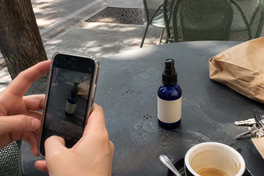 Someone casually photographing an unbranded cobalt-blue bottle on an outdoor café table.