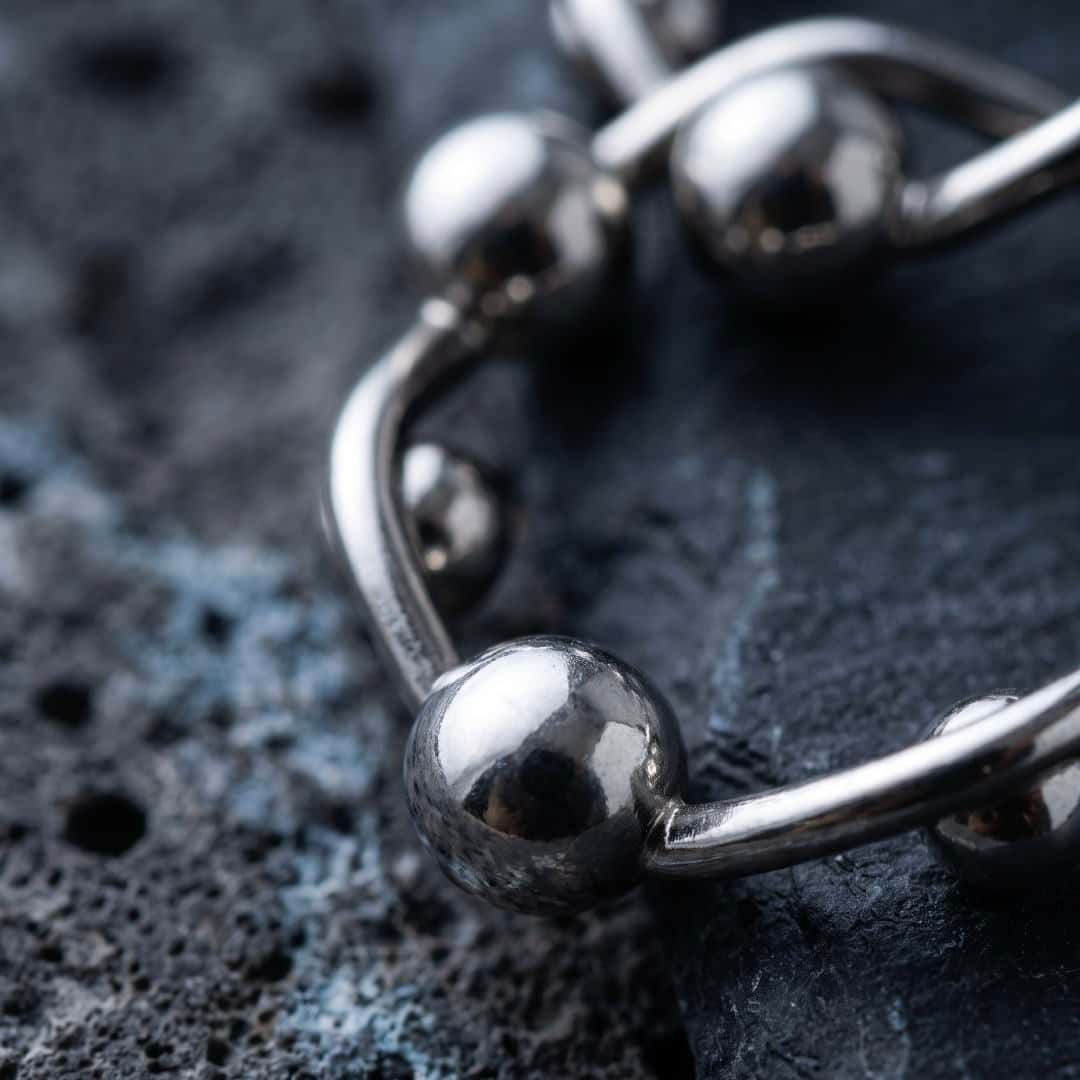 Art-directed close-up of the same silver ball hoop earrings on dark textured stone