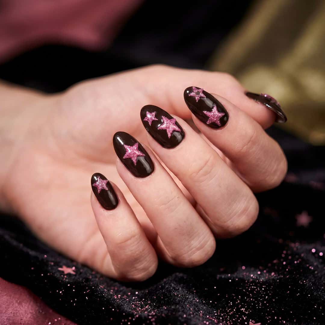 Art-directed close-up of the same black and pink star nail art against dark fabric