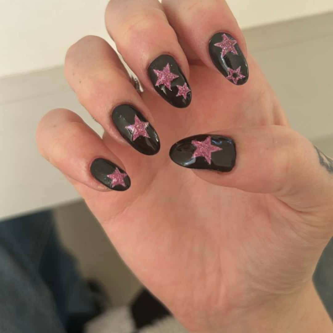 Phone photograph of glossy black nails decorated with pink glitter stars