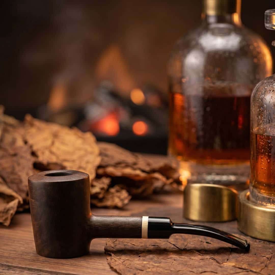 Art-directed photograph of the same dark wood smoking pipe beside amber bottles and a fireplace