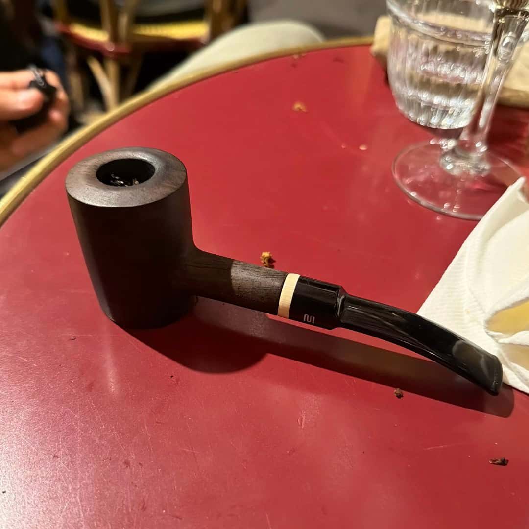 Phone photograph of a dark wood smoking pipe on a red café table